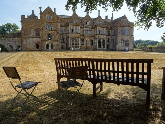 A photograph of Broughton Castle with a bench and chairs in the foreground